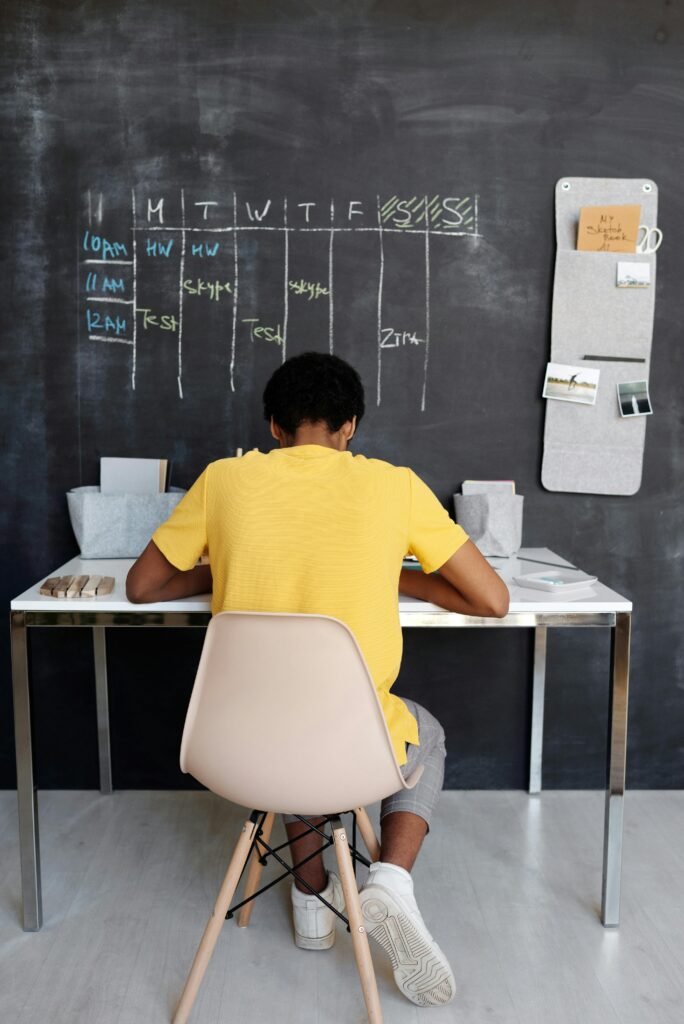 Junge von hinten am Schreibtisch mit Kreidetafel und Stundenplan vor ihm