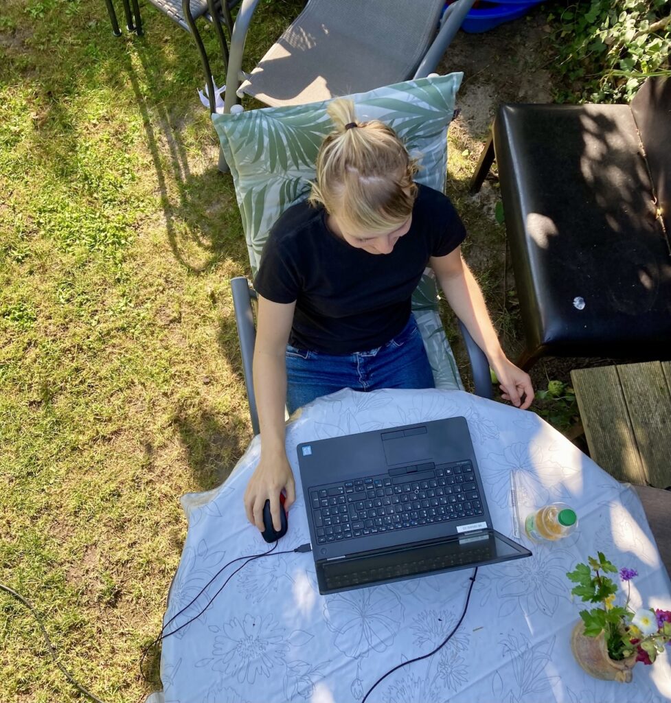 Frau sitzt im Garten am Laptop und wird von oben fotografiert