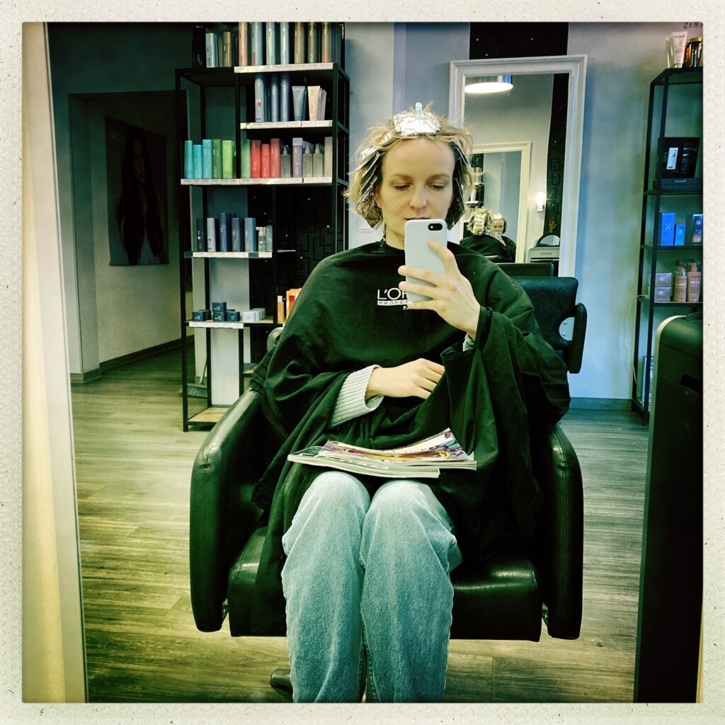 Selfie beim Friseur mit Smartphone und Magazinen