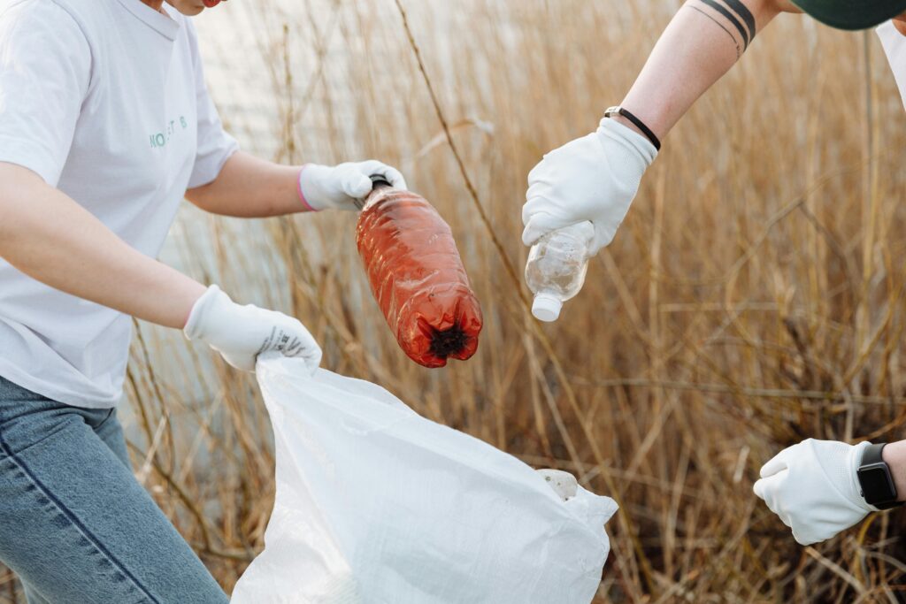 zwei Personen sammeln Plastikflaschen in der Natur mit Handschuhen