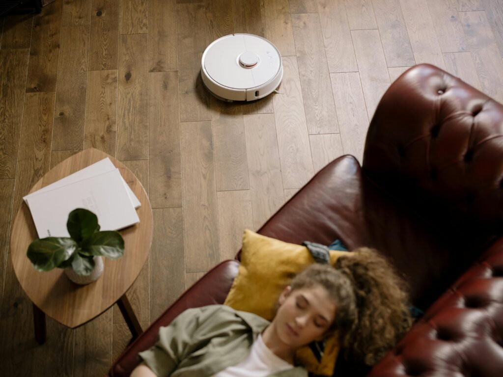 Frau liegt auf der Couch während Staubsaugerroboter saugt